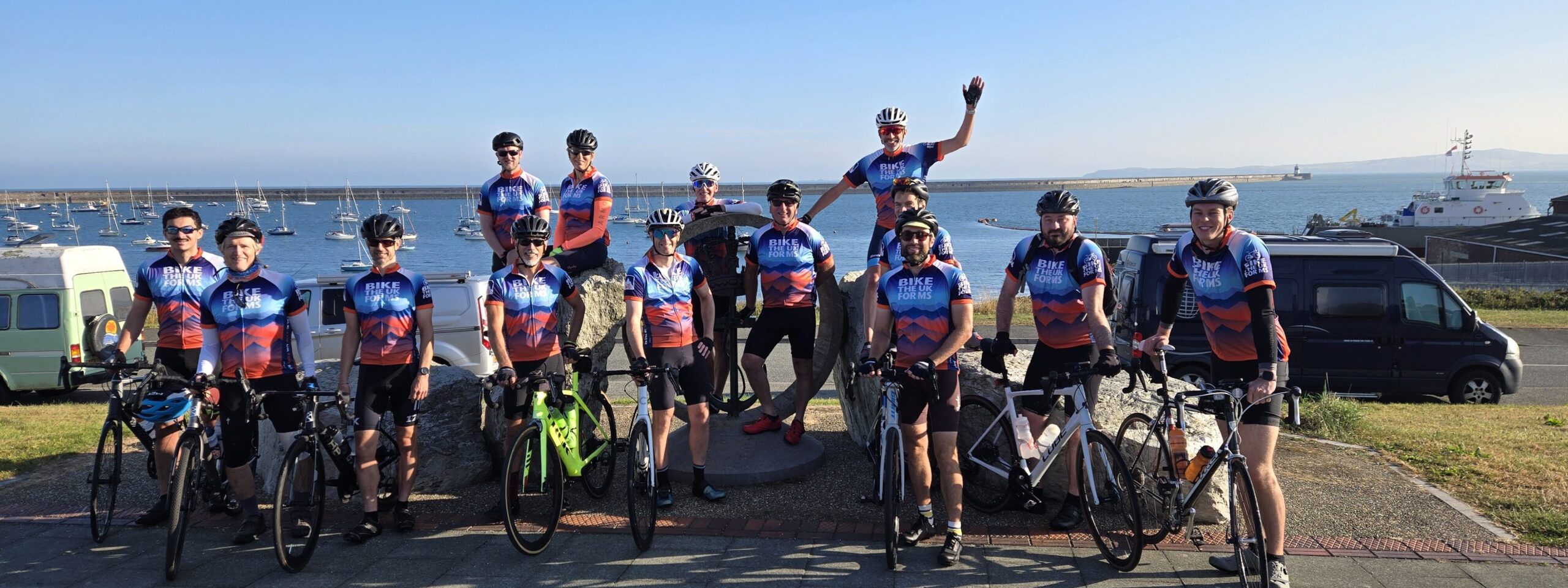 Riders in front of the water smiling for the camera before setting off on Lon Las Cymru