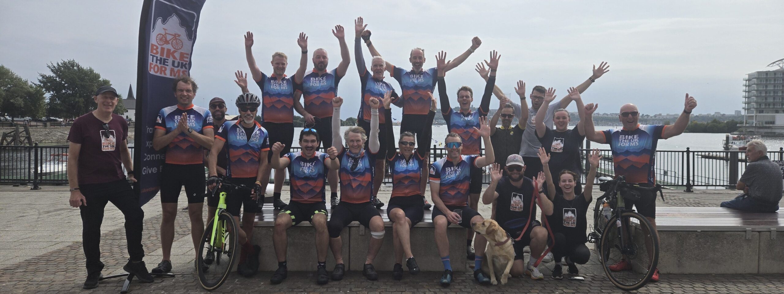 Riders in front of the sea in Cardiff smiling and cheering after completing their Lon Las Cymru journey