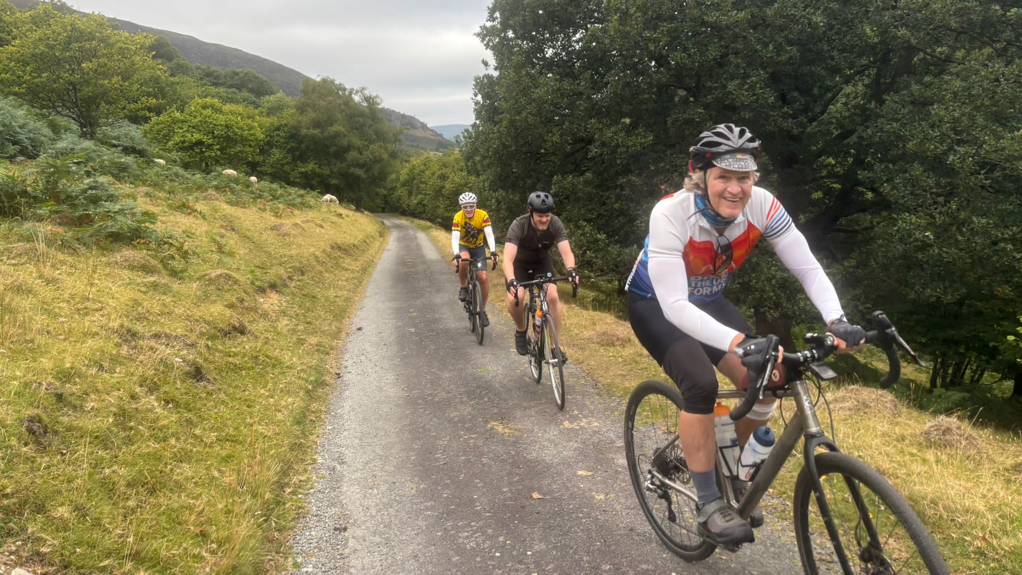 3 cyclists riding up a hill, smiling at the camera 